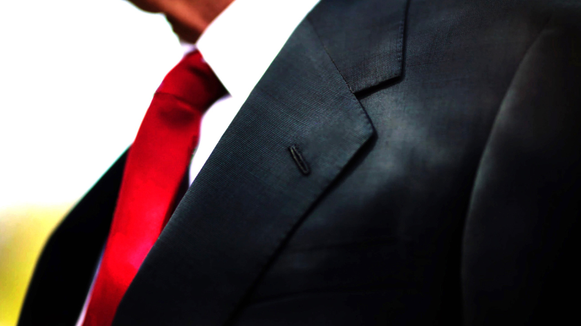 A man in a black suit, with a red tie, and a orangey-tanned neck jowl