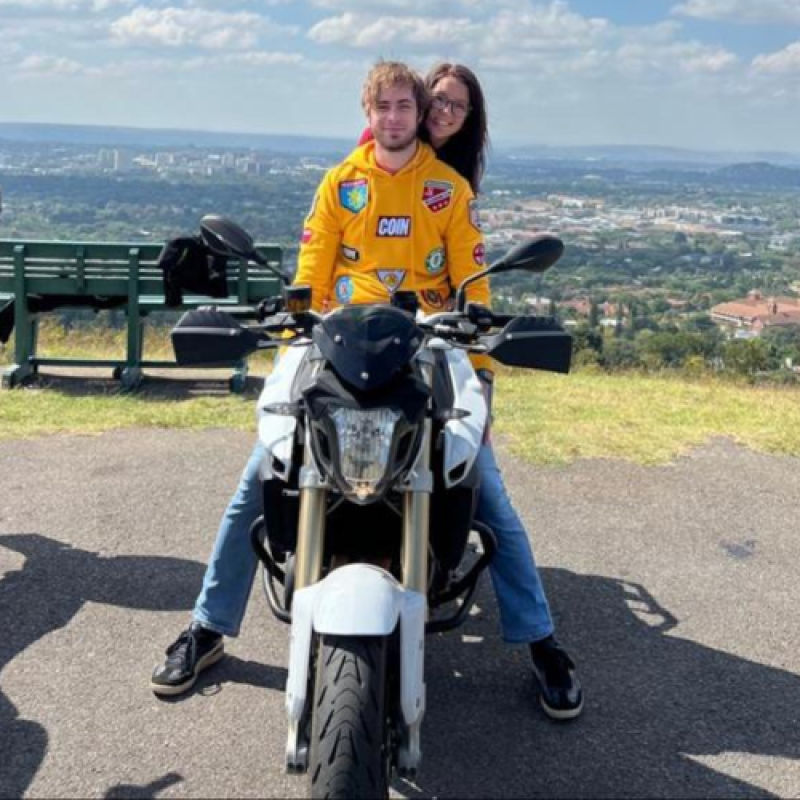 Ruan Crouse sits on a motorcycle, with his girlfriend behind him overlooking a cityscape